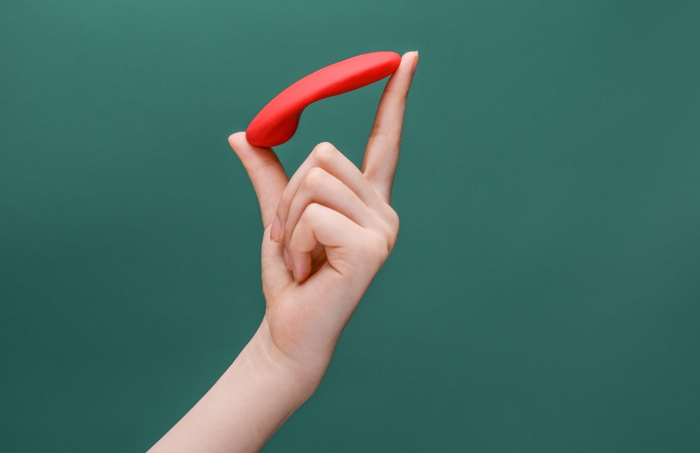 Hand balancing a red curved vibrator against a green background.