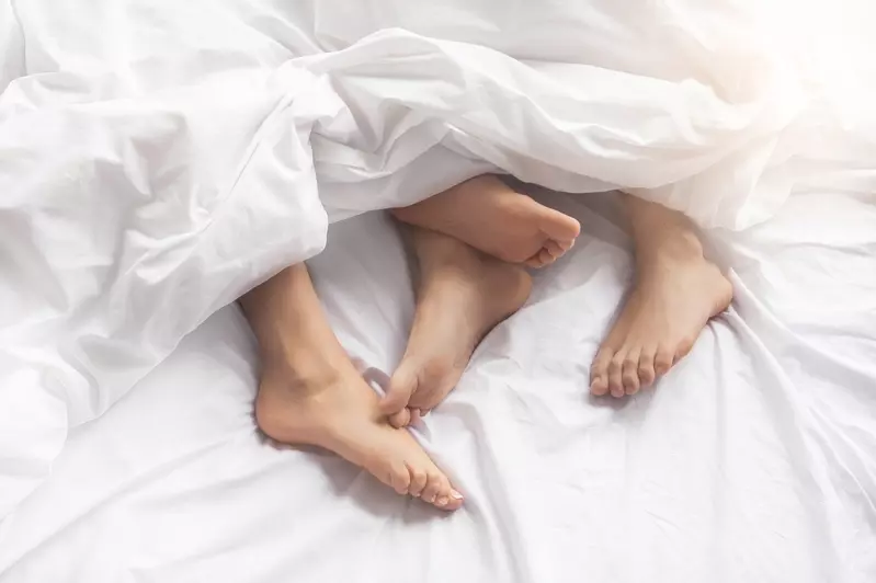 Two pairs of feet under white bed sheets.