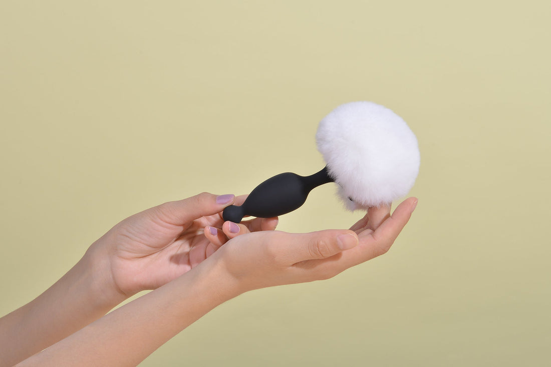 Hand holding a black plug with a white fluffy tail.