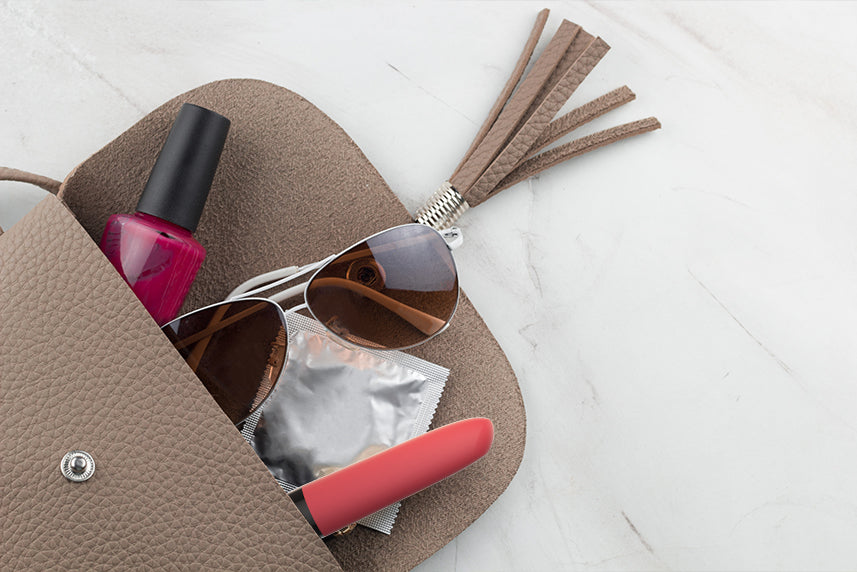 Open handbag with sunglasses, a condom packet, nail polish, and a red vibrator.