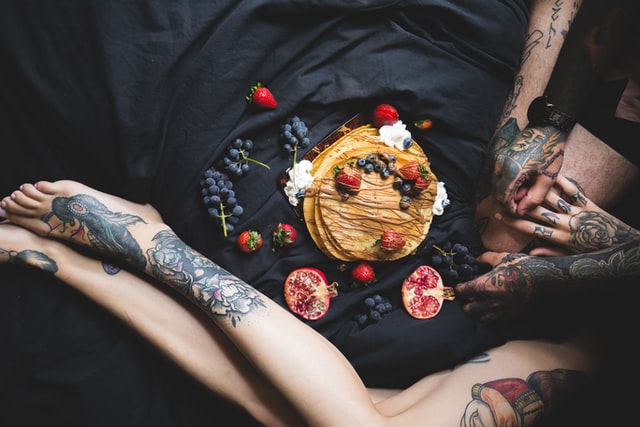 Tattooed couple beside a dessert topped with fruit.