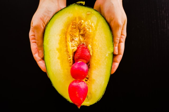 Hands holding a halved melon filled with red fruit.