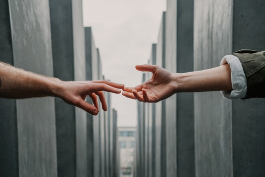 Two hands reaching toward each other between concrete walls.