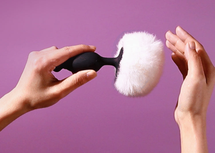 Hands holding a black butt plug with a white fluffy attachment.