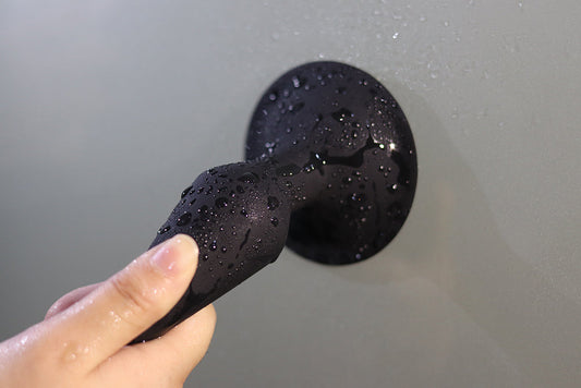 Hand holding a black butt plug covered in water droplets.