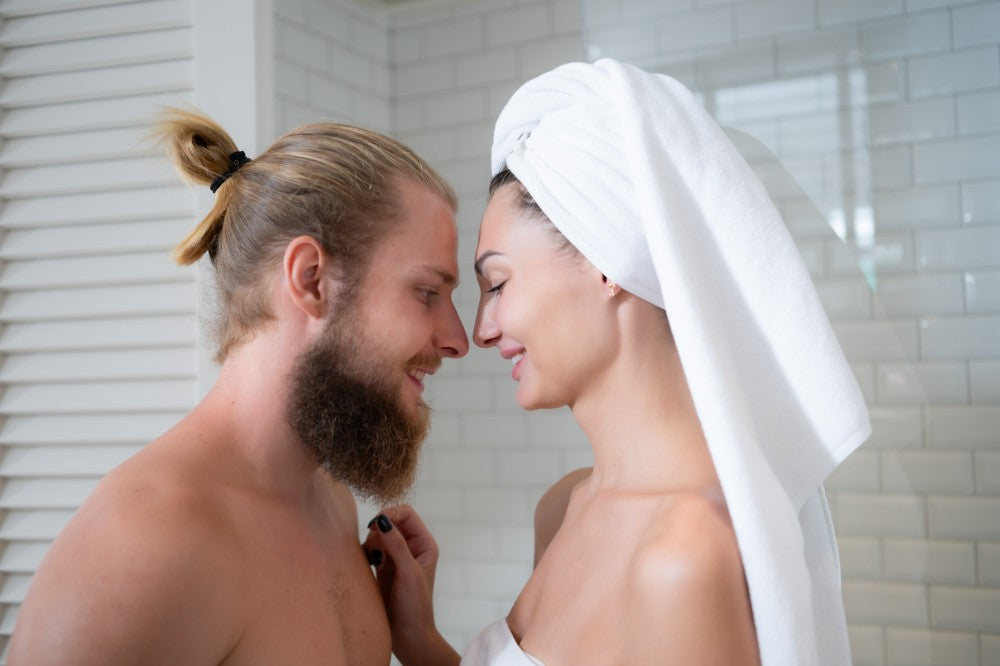 Couple smiling together in a bathroom with a towel.