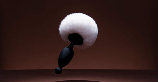 Black butt plug beside a white fluffy cushion.