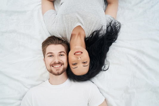 Smiling couple lying together on white bed sheets.