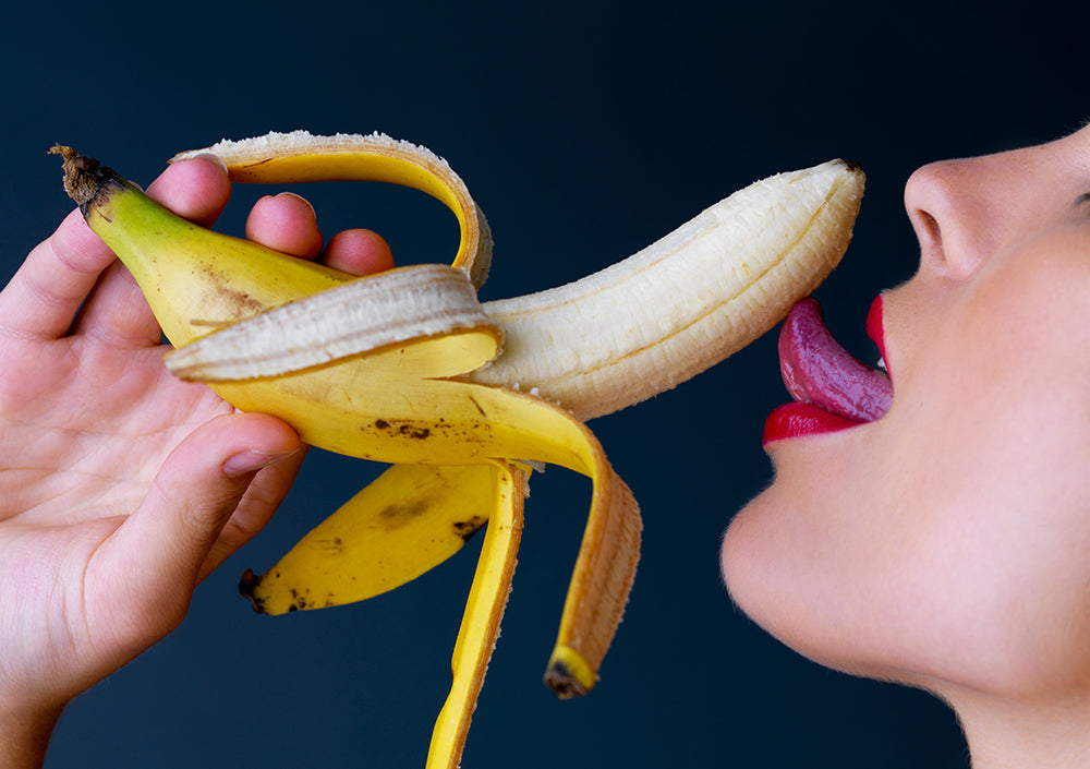 Close-up of a person holding a peeled banana near their mouth.
