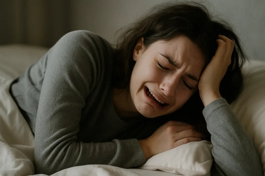 Woman lying in bed while crying and holding her head.