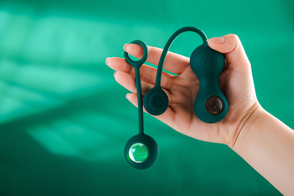 Hand holding green Kegel exercisers against a green background.