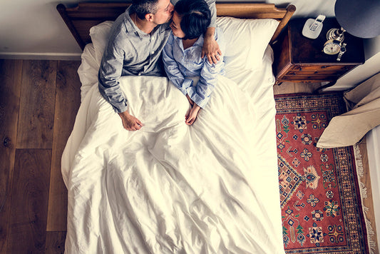 Couple kissing in bed, viewed from above.