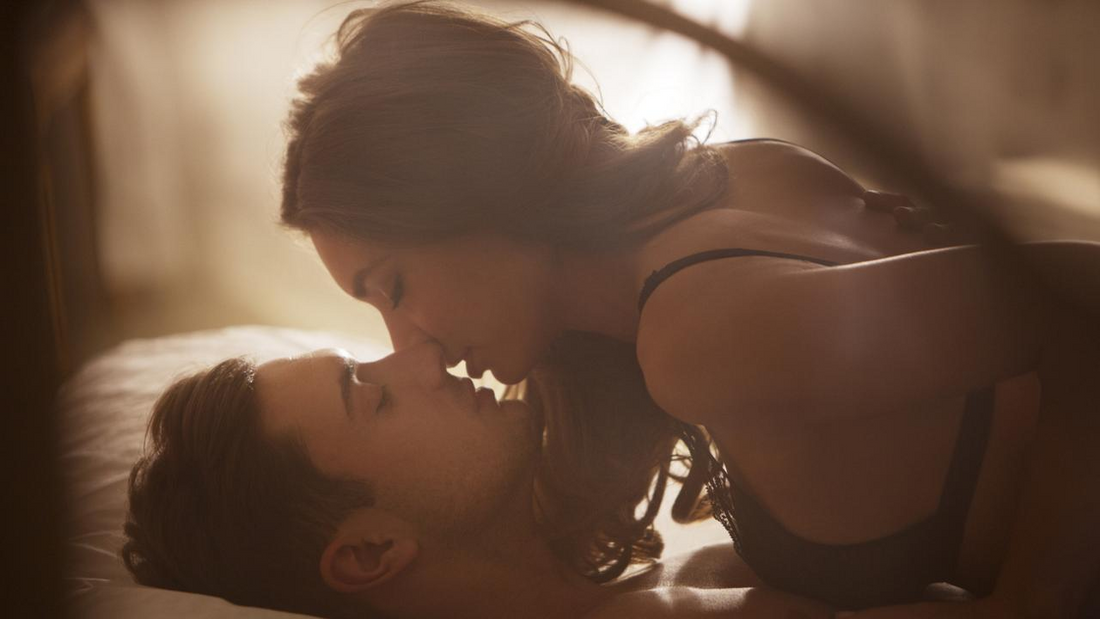 Couple leaning in for a kiss on a bed.