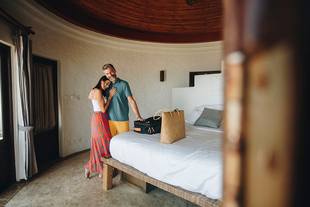 Couple standing together in a hotel room beside packed luggage.