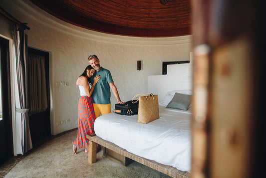 Couple standing together in a hotel room beside packed luggage.