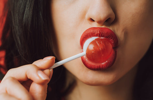 Close-up of red lips holding a lollipop.