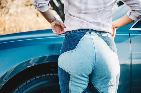 Back view of a person in patchwork jeans beside a blue car.
