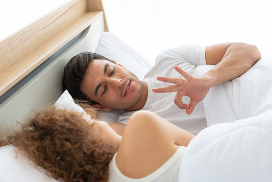 Couple lying in bed while one person makes an OK gesture.