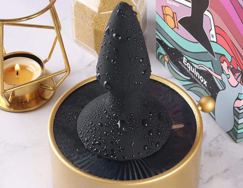 Black butt plug beside a candle and product box.