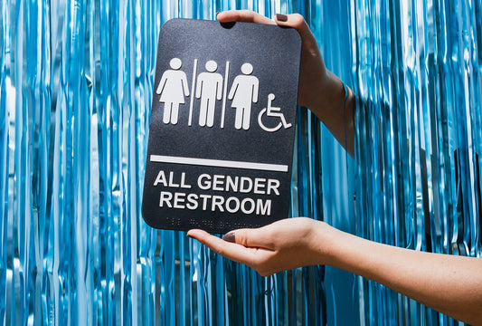 Hands holding an all-gender restroom sign against blue streamers.