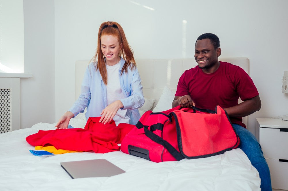 Couple packing luggage together on a bed.