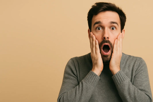 Surprised man holding his cheeks against a beige background.