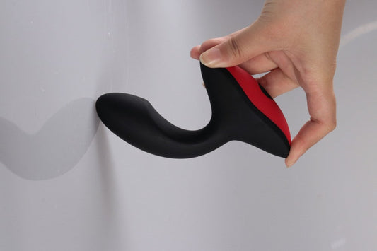 Hand holding a black and red prostate massager against a white background.