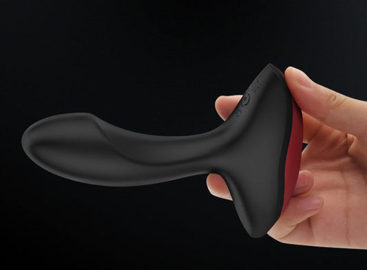Hand holding a black prostate massager on a dark background.