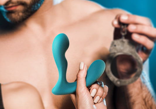 Teal prostate massager held in front of a handcuff and bare chest.