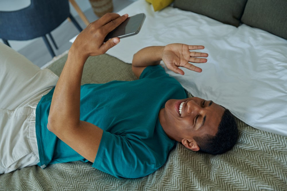 Man smiling at a smartphone while lying on a bed.
