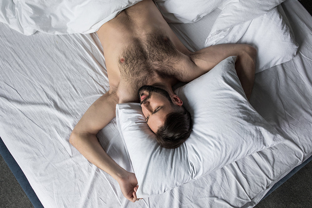 Shirtless man resting in white bed sheets.