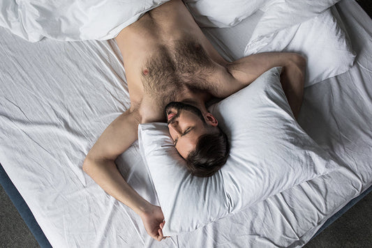 Shirtless man resting in white bed sheets.