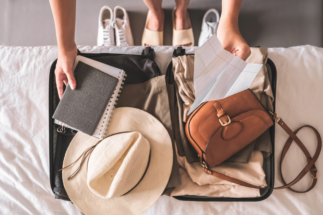 Open suitcase packed with clothes, a hat, notebook, and travel bag.
