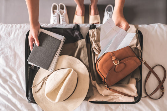 Open suitcase packed with clothes, a hat, notebook, and travel bag.