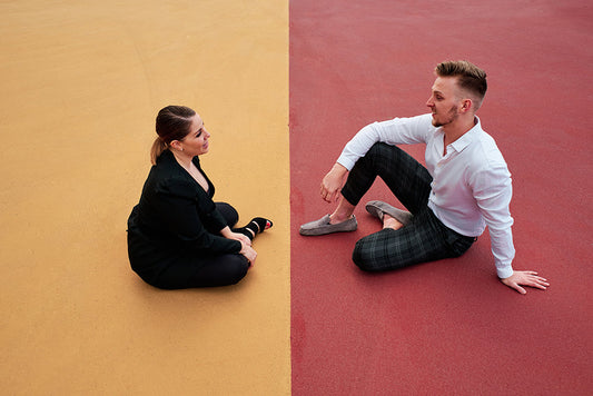 Two people sitting apart on yellow and red pavement.