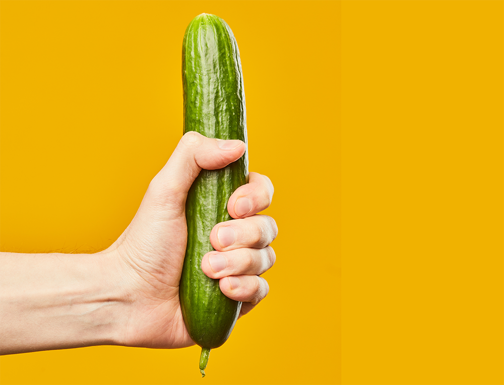 Hand holding a cucumber against a yellow background.