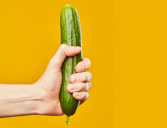 Hand holding a cucumber against a yellow background.