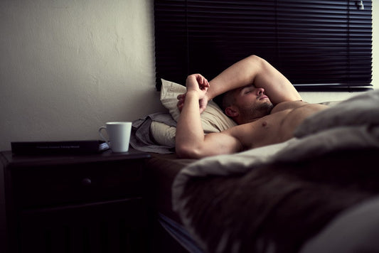 Shirtless man lying awake in bed.