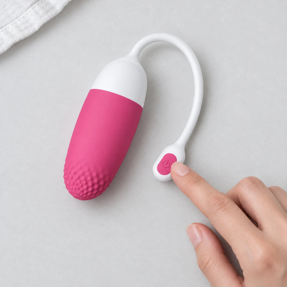 Hand touching the pink button on the white tail of a Magic Vini